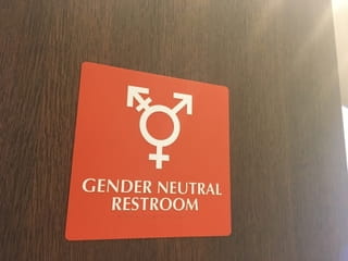 Bord voor een genderneutraal toilet met gecombineerde symbolen voor man en vrouw op een rode achtergrond, met de tekst 'GENDER NEUTRAL RESTROOM'.