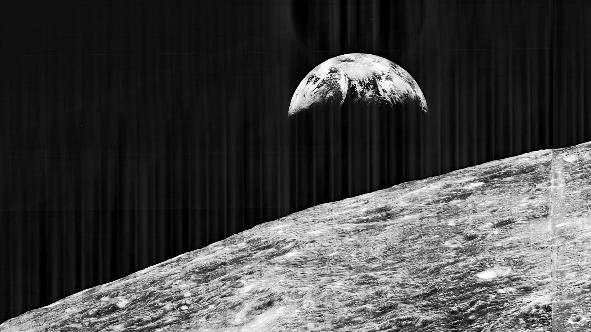Zwart wit foto van de aarde, met op de voorgrond het maanoppervlak. Deze foto is genomen door de Lunar Orbiter 1, die het maanoppervlak in kaart moest brengen voor de Apollo landingen.  