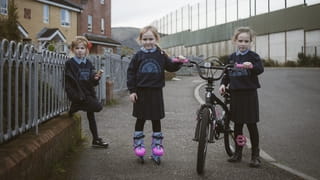 Drie meisjes voor hun huizen naast de vredesmuur in Iers Republikeins gebied, Belfast. 