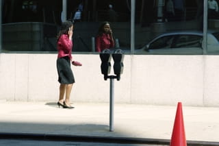 vrouw met roze blouse, roze handtas, zwarte rok en dito gekleurde pumps kijkt in de spiegel met heel veel zelfvertrouwen