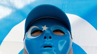 Een Oeigoer moslim met een blauw masker op staat voor een blauw met witte vlag.
