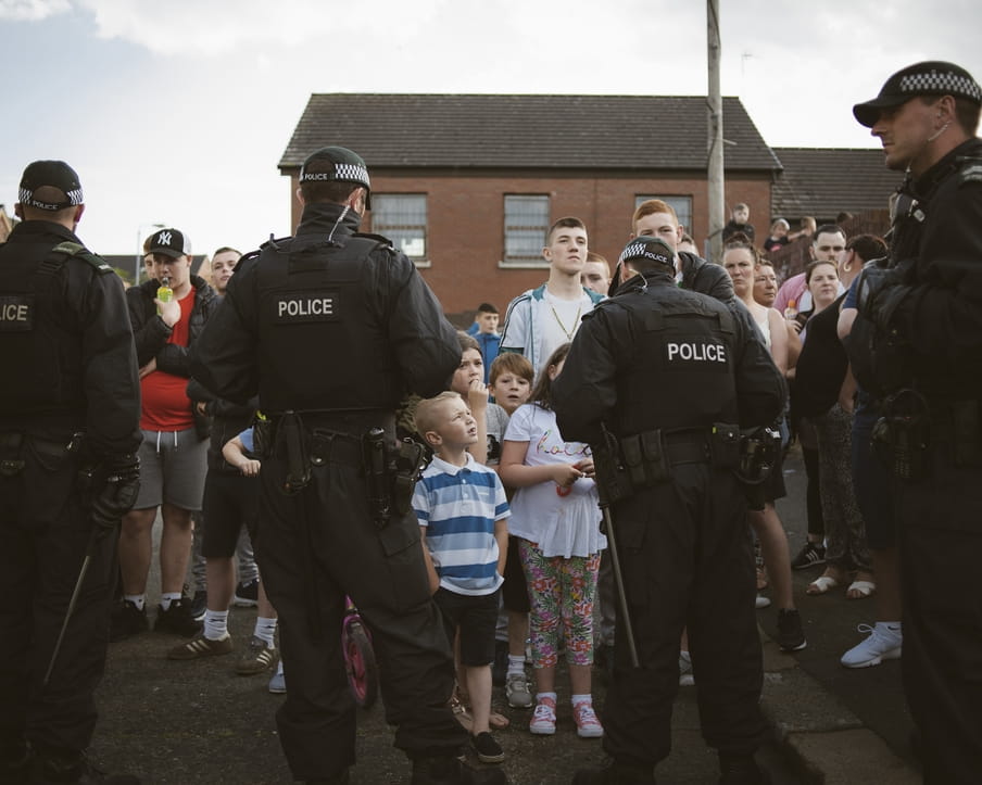 Vanaf hun rug zie je hoe politieagenten katholieke jongeren tegen houden tijdens een Oranjemars op 12 juli 2017 in Belfast. 
