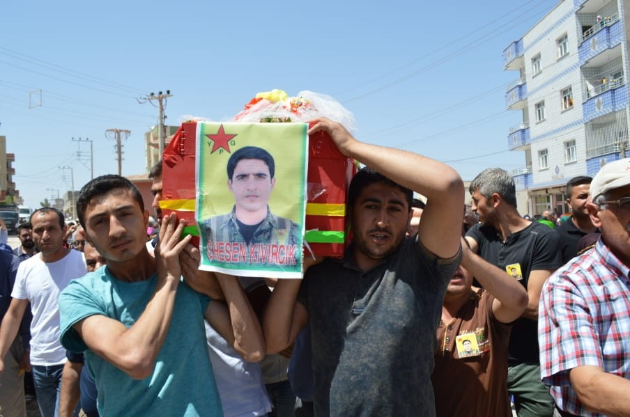 ‘De vuurrode houten kist, met de gele YPG-vlag eroverheen, wordt voorzichtig door de broers en vrienden van Tayfun op de schouders gehesen.’ Foto: Tan Tunali