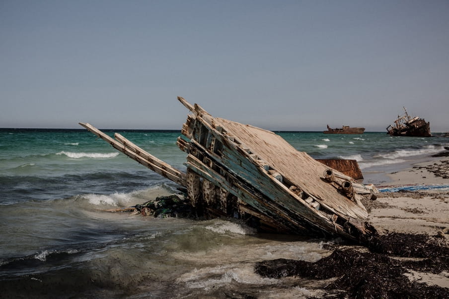 De overblijfselen van een vluchtelingenboot liggen op het strand van Zuwara op 17 augustus 2016, Libië. Zuwara was een van de belangrijkste vertrekpunten voor vluchtelingen die naar Europa werden gesmokkeld, maar omdat de gemeenteraad mensensmokkel in 2015 verbood is Zuwara overgegaan op diesel- en oliesmokkel. De mensensmokkel heeft zich verplaatst naar de dichtbijgelegen plaats Sabartah. Foto: Daniel Etter / Redux