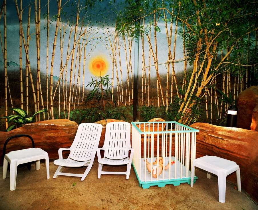 Baby ligt in box voor een afbeelding op de muur geschilderd van een bos met bamboe