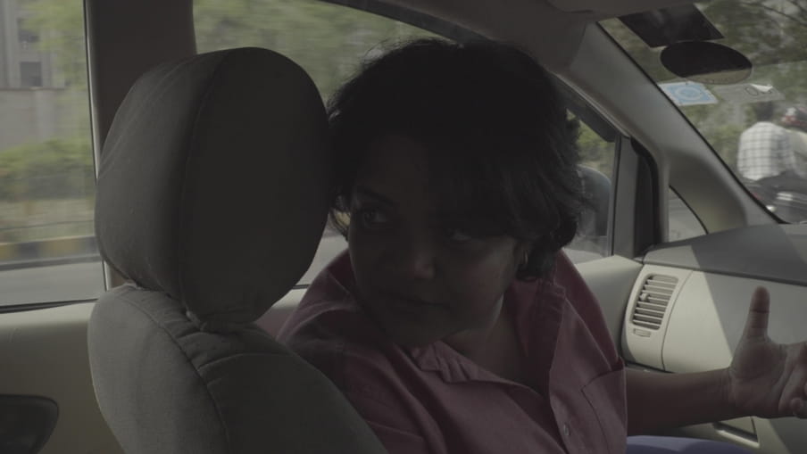 Sandhya Ravishankar wacht achter het stuur in haar auto terwijl ze druk in gesprek is met een bijrijder.