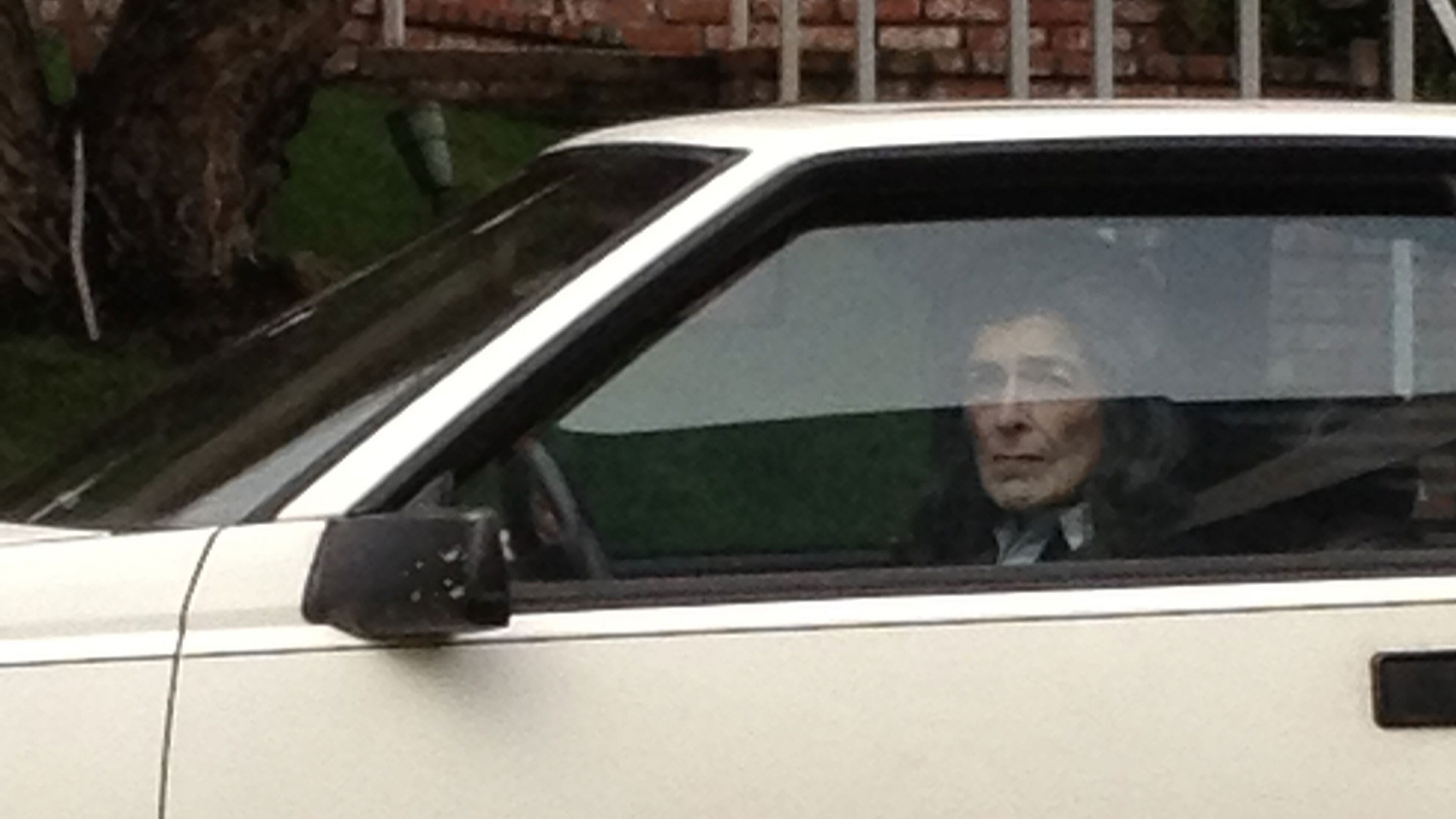 Een gepixelde foto van een vrouw die uit een autoraam kijkt vanuit een witte auto.
