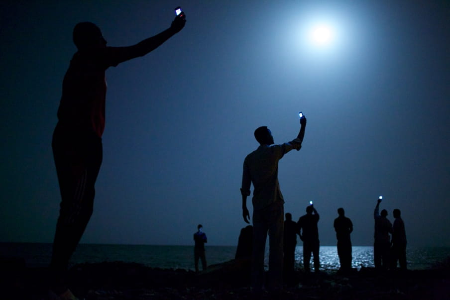Afrikaanse migranten aan de kust van Djibouti steken telefoons in de lucht in de hoop het telefoonsignaal van buurland Somalië op te vangen om zo contact te krijgen met familie in het buitenland. Foto: John Stanmeyer (VII for National Geographic)