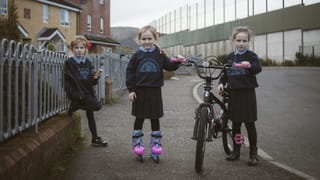 Drie meisjes voor hun huizen naast de vredesmuur in Iers Republikeins gebied, Belfast. 