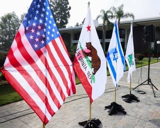 Naast het podium waar hij spreekt staan naast de Amerikaanse vlag, ook de vlag van California, de Israelische vlag en de Appeal to Heaven vlag. Bron: Paul Archuleta/Getty